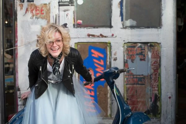 Foto für Tinder. Eine Frau trägt eine Lederjacke und posiert mit einem Vespa.